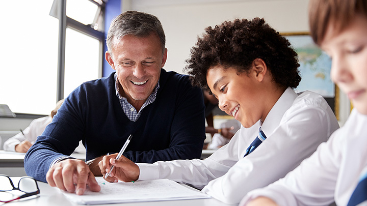 High school teacher giving male student one to one help at desk