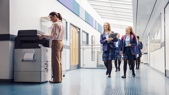 Group of female high school students walking down the school hall with books and laptops in their arms